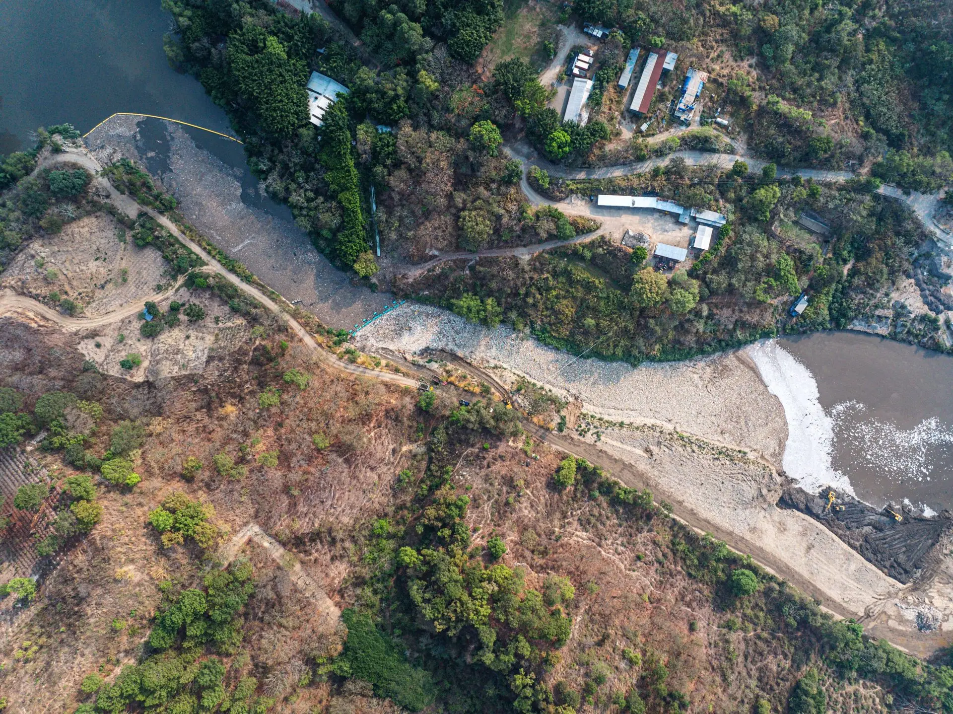 Vista del río Las Vacas en Guatemala con una barrera interceptora capturando una masa densa de residuos plásticos que avanzan hacia el río Motagua.